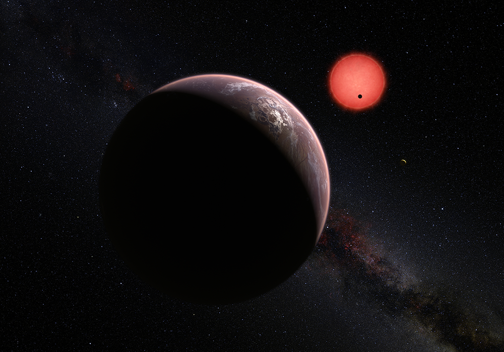 This artist’s impression shows an imagined view of the three planets orbiting an ultracool dwarf star just 40 light-years from Earth that were discovered using the TRAPPIST telescope at ESO’s La Silla Observatory. These worlds have sizes and temperatures similar to those of Venus and Earth and may be the best targets found so far for the search for life outside the Solar System. They are the first planets ever discovered around such a tiny and dim star.
In this view one of the inner planets is seen in transit across the disc of its tiny and dim parent star. (Credit: ESO/M. Kornmesser/N. Risinger (skysurvey.org))